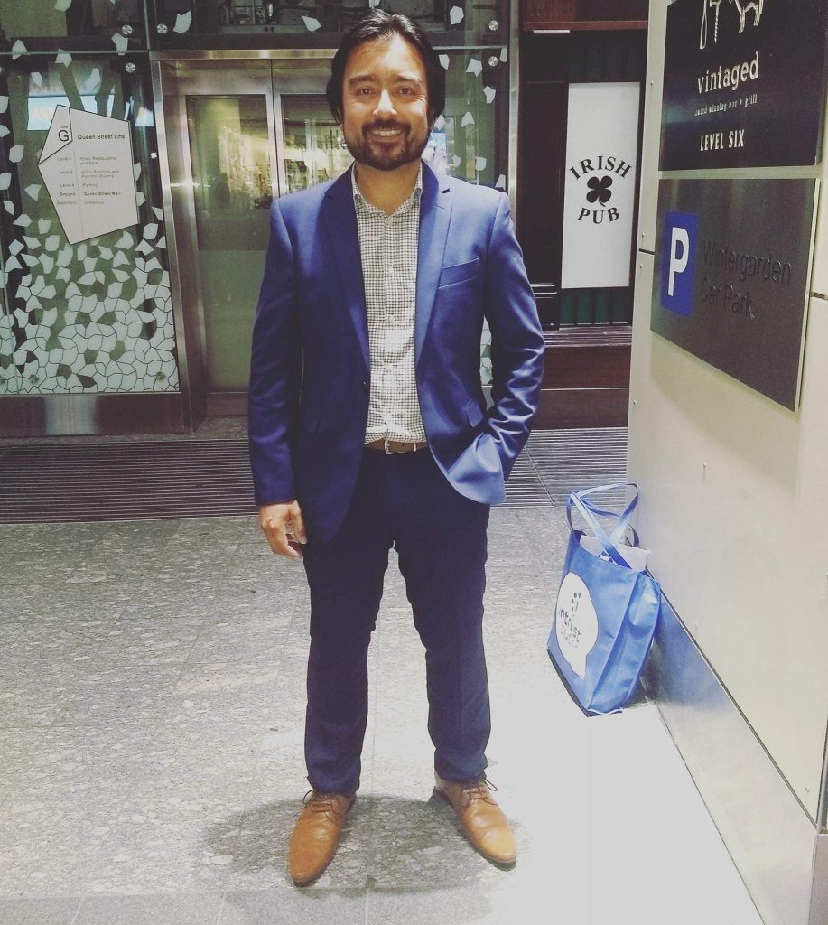 Aaron in a blue suit outside a shop.